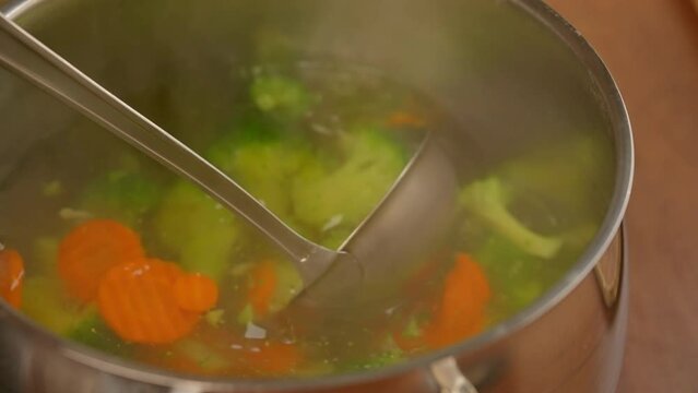 woman cooking soup for lunch holding ladle colorful vegetables hot and healthy soup vegetarian meal slow motion