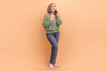 Full length photo of funny woman wear khaki cardigan arm on chest talk on smartphone look empty space isolated on beige color background