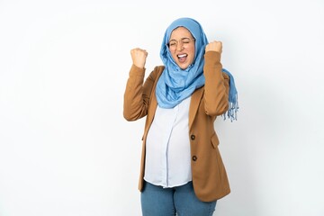 Young beautiful pregnant muslim woman wearing hijab over white background being excited for success with raised arms and closed eyes celebrating victory. Winner concept.