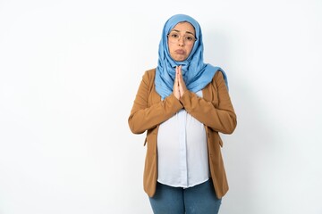 Positive Young beautiful pregnant muslim woman wearing hijab over white background smiles happily, glad to receive pleasant news from interlocutor, keeps palms together, People emotions concept.