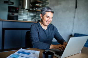 Fototapeta premium Middle aged man working on his laptop and going over his bills at home