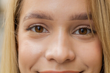 Extreme close-up macro portrait of face. Young adult beautiful blonde woman's eyes looking at camera. Brown eyes of teen girl female. Caucasian woman opening blinking eyes, smiling. Laser correction
