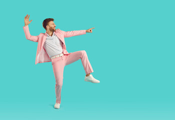 Portrait of a young happy funny man wearing bright pink suit having fun and dancing isolated on a...