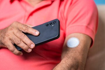 Close up shot of senior man checking sugar or glucose level by tapping mobile phone to sensor at home - concept of technology, diabetes and health care