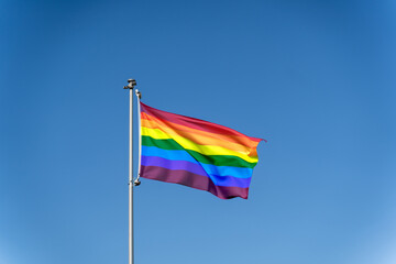 LGBTQ rainbow flag waving against a clear blue sky