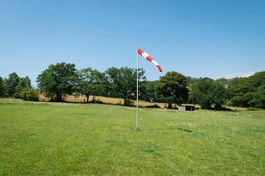 Cone girat&oacute;rio que indica a dire&ccedil;&atilde;o do vento colocado num locar de pouso para a pr&aacute;tica de paraquedismo a meio a algumas &aacute;rvores e verde relva