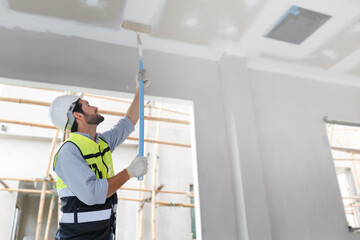 Male painter with paint roller forward on the construction site White primer on concrete walls...
