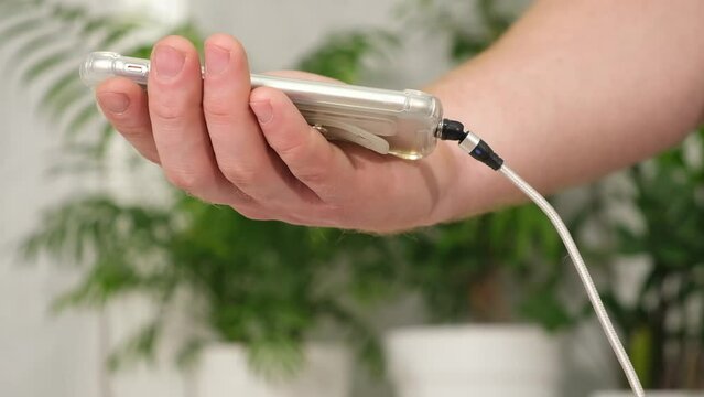 Man's hand connects magnetic cable for charging smartphone on a white background.