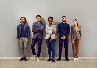 Portrait of joyful multiracial colleagues of successful business team standing in row in office. Smiling Caucasian and African American men and women in smart casual clothes posing near gray wall. - Powered by Adobe