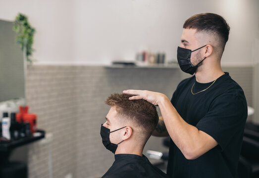 Young hairdresser with mask cutting hair in barber shop