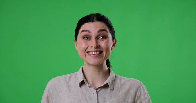 Portrait of a cheerful Caucasian woman standing over green screen background. She looking at camera, and suddenly sees something amazing, exclaiming Wow She then smiles and laughs joyfully.