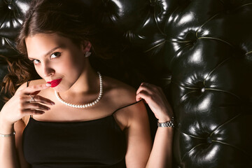 elegant well dressed sensual girl posing on a shiny black leather couch with bright red lipstick.