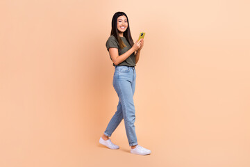 Fototapeta na wymiar Full body length cadre of young japanese model using her apple smartphone for searching cheap tickets airplane isolated on beige background