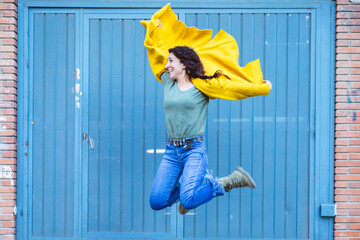 Woman in yellow coat takes a leap with a positive attitude in front of a blue door