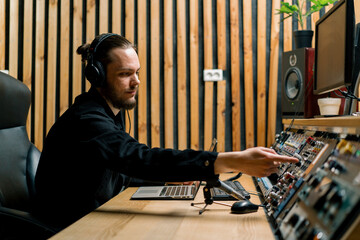 young sound engineer with headphones working in a music studio with monitors and an equalizer...