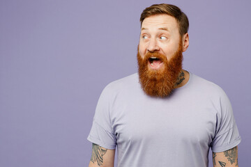 Young surprised shocked redhead bearded man wear violet t-shirt casual clothes look aside on workspace area mock up isolated on plain pastel light purple background studio portrait. Lifestyle concept.