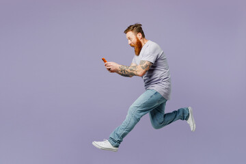 Full body young redhead bearded man wear violet t-shirt casual clothes jump high hold in hand use...