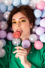 portrait face shot, attractive beautiful girl stylish with bright makeup and double bun hair, emotional, facial expression, lying in a pool filled with pastel multi colored plastic balls, top view.