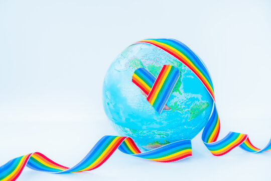 Earth globe model with LGBT rainbow ribbon and heart on the white background. LGBTQIA Pride Month concept. Lesbian gay bisexual transgender. Gender equality. Human rights and tolerance. Copy space