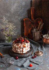 Homemade meringue cake with cherries and chocolate syrup on a dark background surrounded by vintage crockery and flowers - 611049058