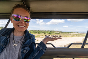 Forced perspective composition of a woman in a safari vehicle pretends to hold a herd of elephants