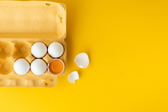 Flat lay of white eggs in the carton brown box on the yellow background. Top view of broken egg with white shell. Copy space for a free text.