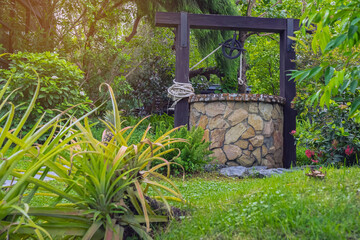 Beautiful artesian well made by stones and wheel pulley with metal bucket and rope in peaceful...
