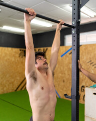 Moustached, shirtless young man in good physical shape gripping the top bar of the training box before starting the exercise at the training center.