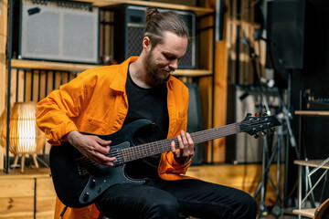 portrait of young rock artist with electric guitar in recording studio playing own track musical instrument drums on background
