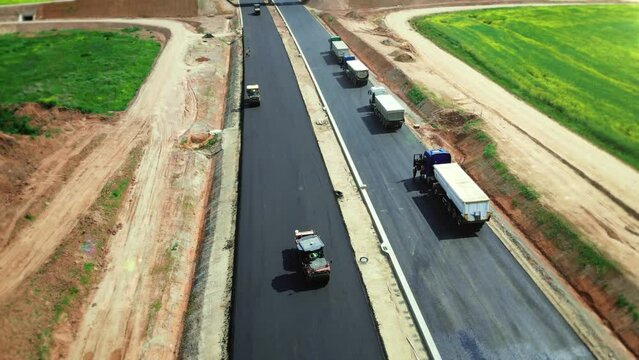 Aerial view of road construction. Asphalt pavers lay asphalt at the construction site of a new wide highway with a bridge. Road rollers drive on a new road. Roadway repair. Heavy machinery. 4k footage