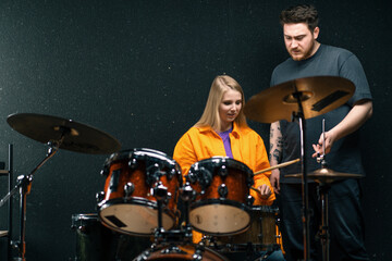young girl in a drum school learns to play a musical instrument with a teacher rehearsing in a band's music studio