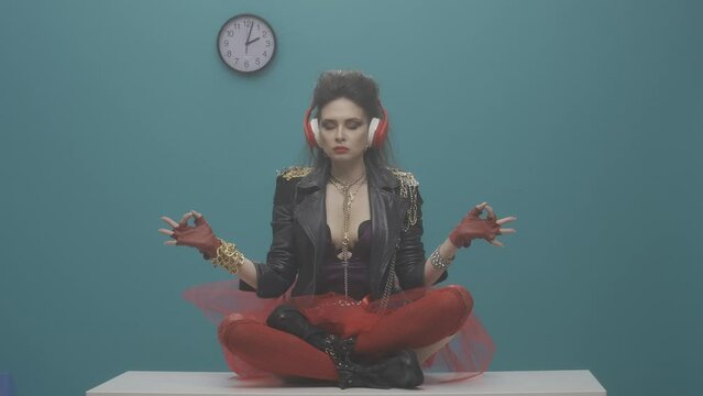A freak woman in headphones sits on a desktop in the office in a lotus position and meditates. The office worker hands her papers, the woman abruptly stops him with a gesture. HDR BT2020 HLG Material