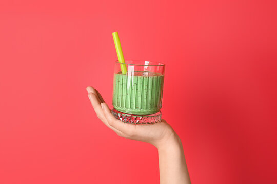 Female hand with glass of green smoothie on red background
