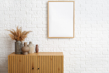 Wooden chest of drawers with vases near white brick wall in room