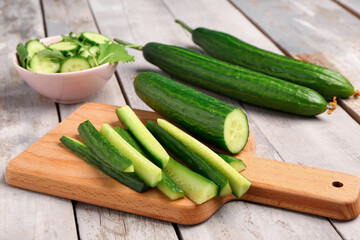Board with fresh cut cucumber on light wooden background
