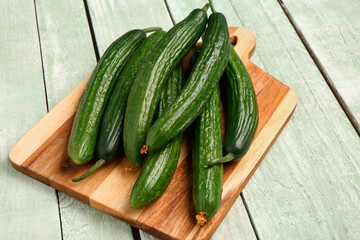 Board with fresh cucumbers on light wooden background
