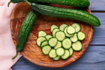 Plate with cut and whole cucumbers on grey wooden background, closeup