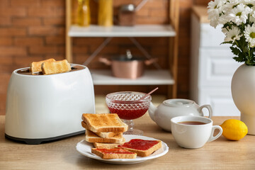 Modern toaster, sweet jam toasts and cup of tea on table in kitchen