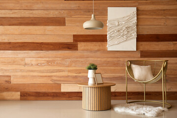 Cozy armchair with cushion and houseplant on coffee table near wooden wall