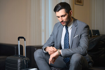 Hotel guest sits on leather sofa and looks at his wristwatch