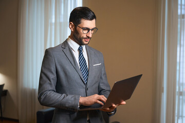 Elegant brunette is standing in a hotel room with laptop