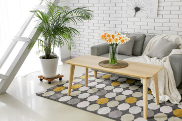 Interior of light living room with grey sofa and narcissus flowers on wooden coffee table