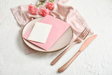 Clean plate with blank invitation card, cutlery and carnation flowers on white table