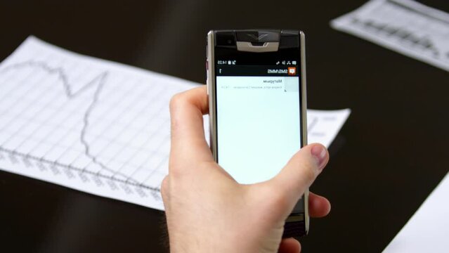 Young man puts cell phone on paper on black meeting table. Manager takes mobile phone in hand and checks incoming message crop body