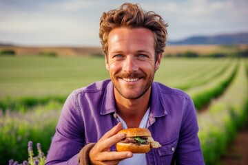 Headshot portrait photography of a satisfied boy in his 30s eating burguer against a lavender field background. With generative AI technology