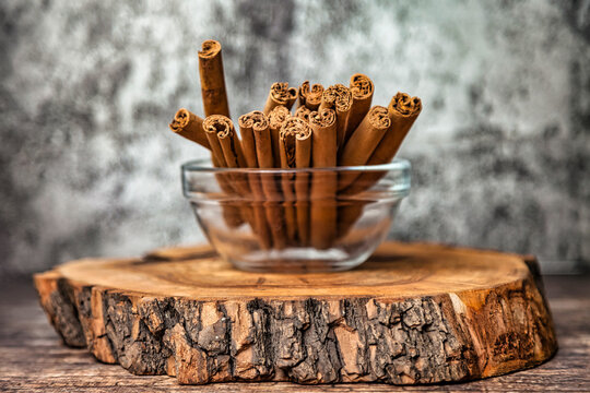 Ceylon Cinnamon Sticks In Glass Plate On Wooden Board, Rustic Style. Still Life Natural Food Of Sri Lankan Cinnamon Sticks On Table At Grey Wall. Delicious Tasty Healthy Concept. Copy Ad Text Space