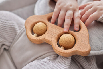 Close-up of a baby s hand, playing with a wooden toy. Unfocused background.
