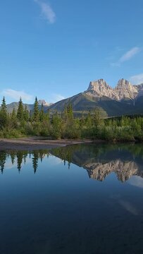 Mountain peaks reflecting in the calm water below at Three Sisters in Canmore, near Banff National Park, Canada in summer time with wilderness, wild, tourist, tourism area.