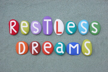 Restless Dreams, creative text composed with multi colored stone letters over green sand
