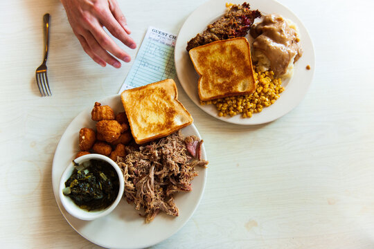 Two plates of barbecue pork and meatloaf on a linoleum diner table. A hand reaches for the check.